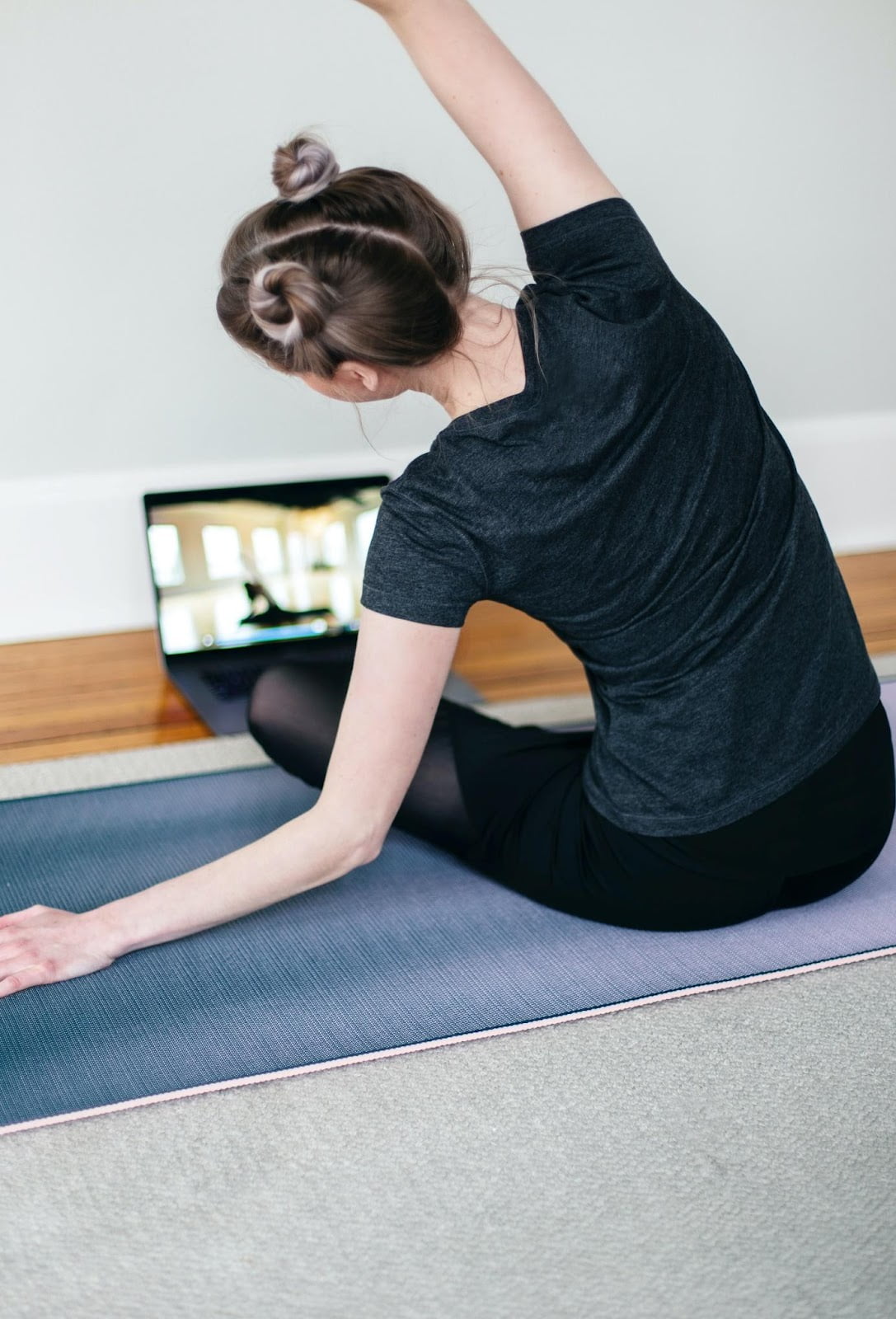 Woman stretching on a yoga mat while following a workout on her laptop
