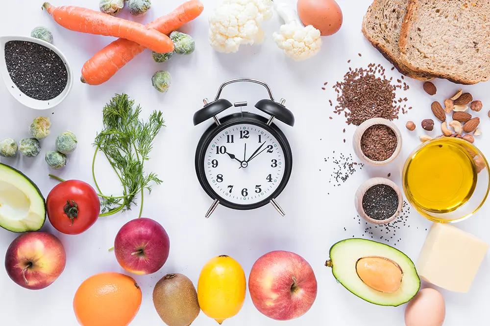Variety of healthy ingredients arranged around an alarm clock on a white background