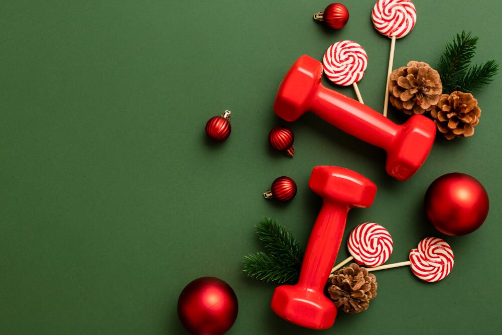 Red dumbbells with Christmas ornaments and candy on a green background