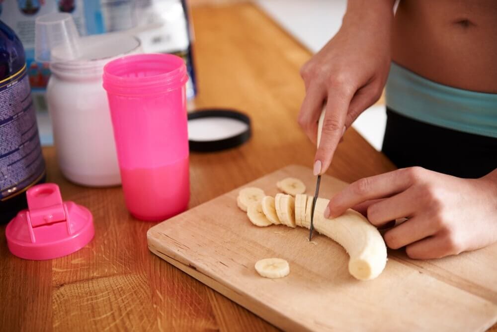 Woman preparing a pre-work out meal, cutting banana for a shake.