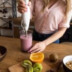 Woman making kiwi, strawberry, orange protein shake.