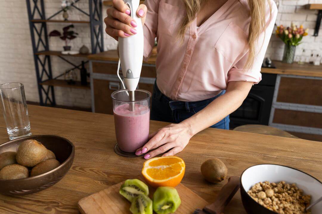 Woman blending a fruit protein shake with kiwi, orange and nuts on the table