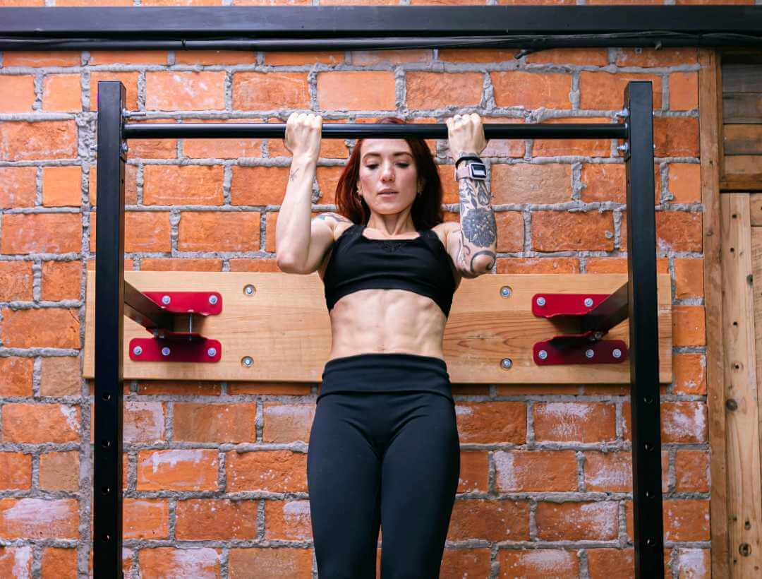 Woman doing pull-ups on a bar in front of a brick wall