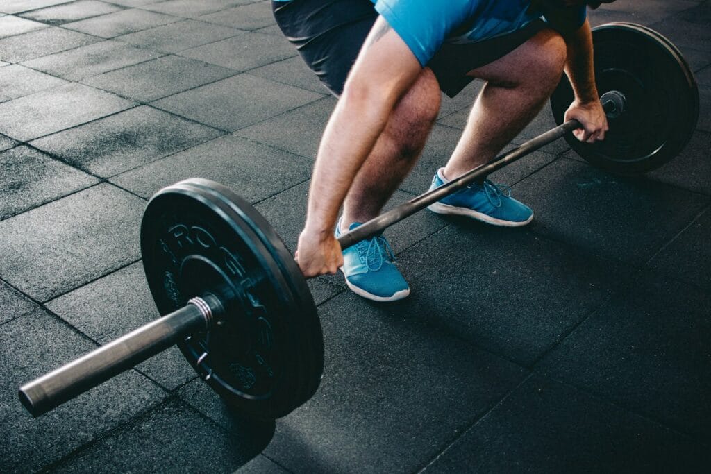 Person gripping a loaded barbell on a gym floor before lifting