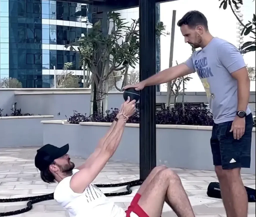 Client doing a weighted sit up outdoors while a Real Fit trainer passes the ball