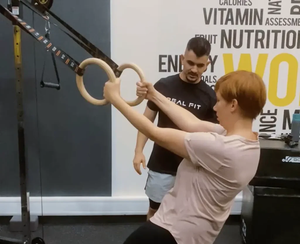 Nejra pulling on gym rings while her Real Fit trainer watches closely