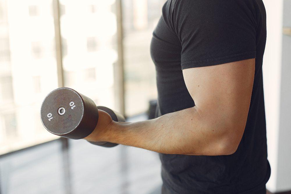 Man in a black t-shirt doing a dumbbell biceps curl, close up