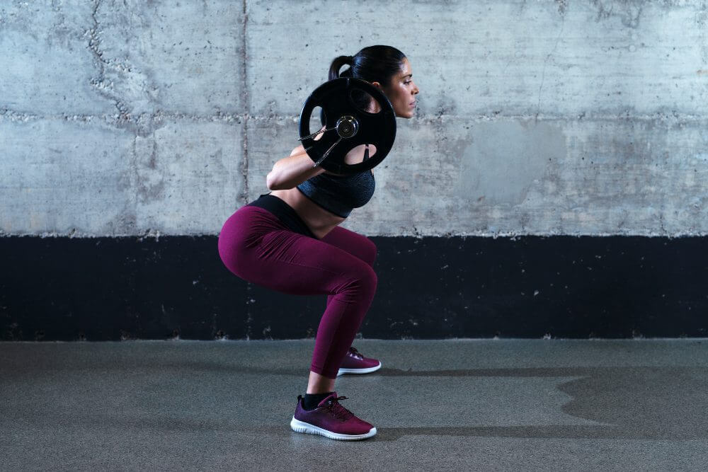 Woman squatting with a barbell on her back against a concrete wall