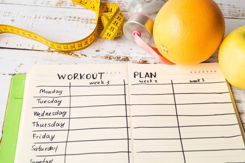 Weekly workout plan notebook beside a measuring tape and grapefruit