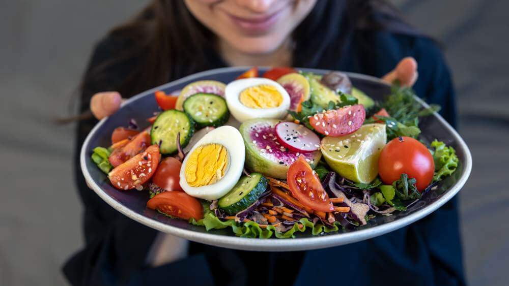 Woman holding a plate of salad with boiled eggs and fresh vegetables