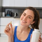 Close up portrait of smiling, healthy young woman, holding tablets, taking vitamin dietary supplements after home fitness workout.