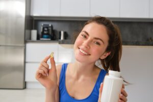 Close up portrait of smiling, healthy young woman, holding tablets, taking vitamin dietary supplements after home fitness workout.