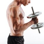 Cropped photo of sweaty bodybuilder lifting dumbbell, isolated on white background