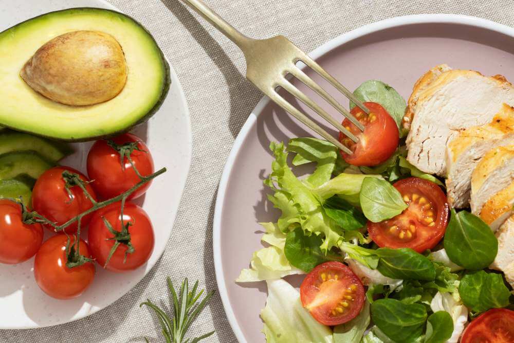 Salad with chicken, tomatoes and leafy greens next to avocado halves