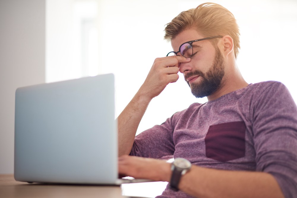 Tired man rubbing his eyes while working on a laptop