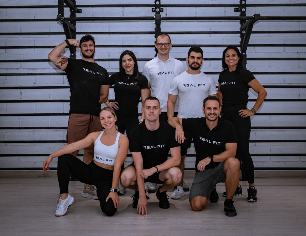 Real Fit personal trainers team posing together in the gym in branded T-shirts