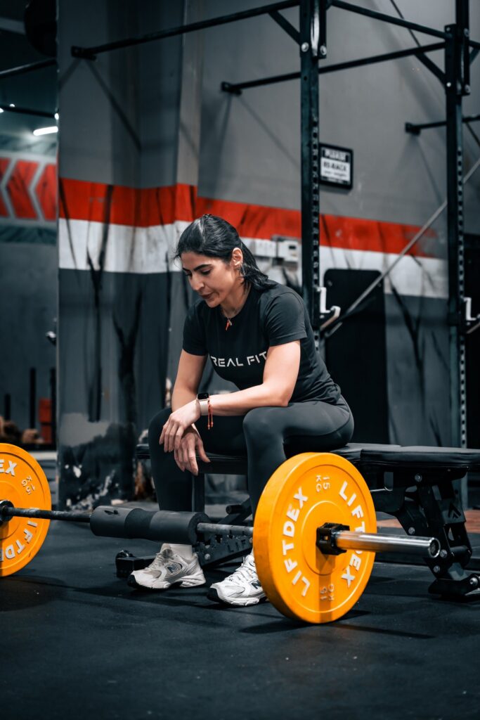 Woman in a Real Fit T-shirt crouching beside a barbell with orange plates in the gym