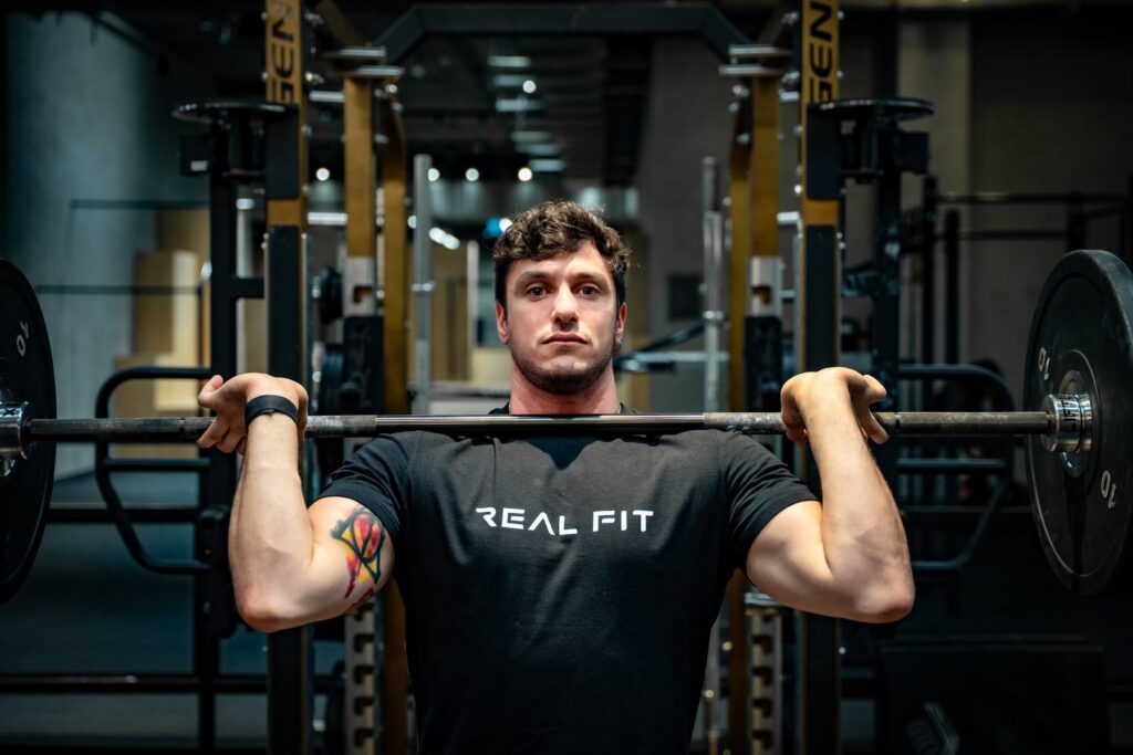 Marcello holding a barbell at shoulder height, facing the camera in the gym