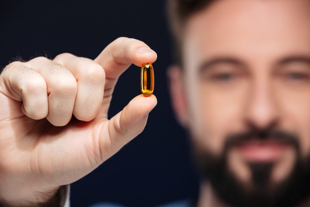 Close up of a young male doctor dressed in uniform with stethoscope showing a pill isolated over dark background