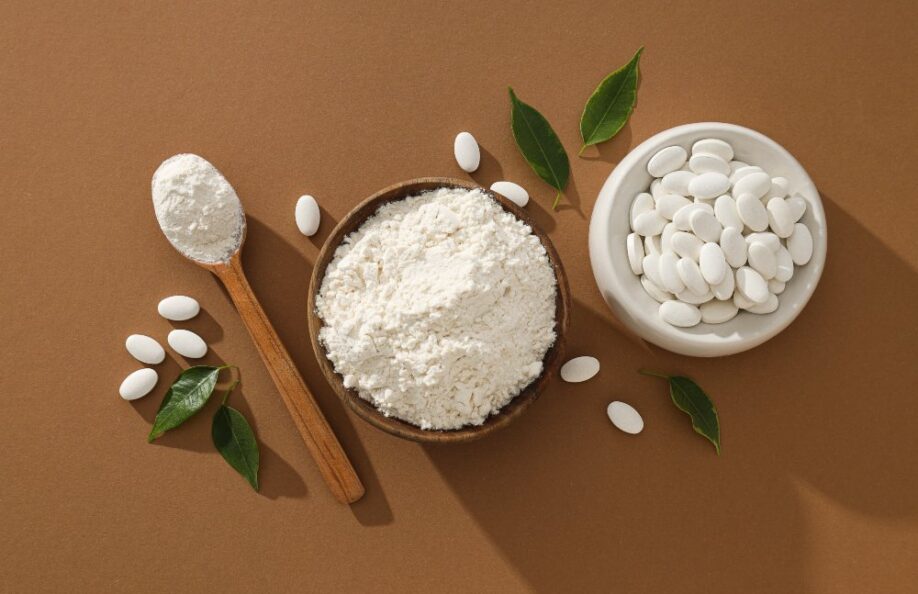 Collagen powder in a bowl and wooden spoon beside a bowl of white tablets