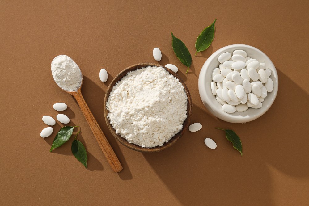 Collagen powder in a bowl and wooden spoon beside a bowl of white tablets