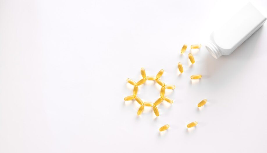 Yellow softgel capsules spilling from a white bottle onto a white surface